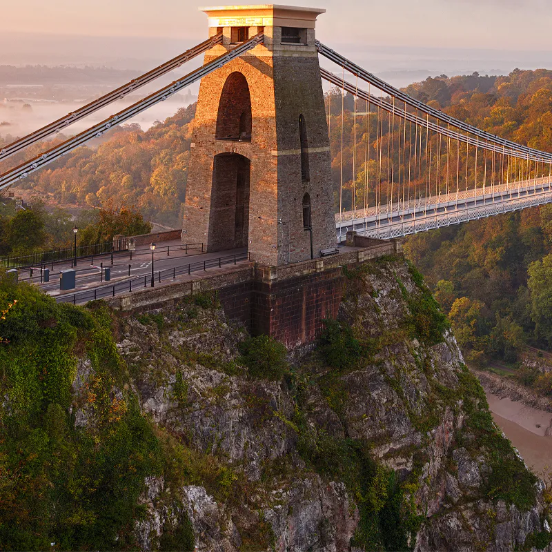 Clifton Suspension Bridge over wooded valley in Bristol, bathed in warm morning light.