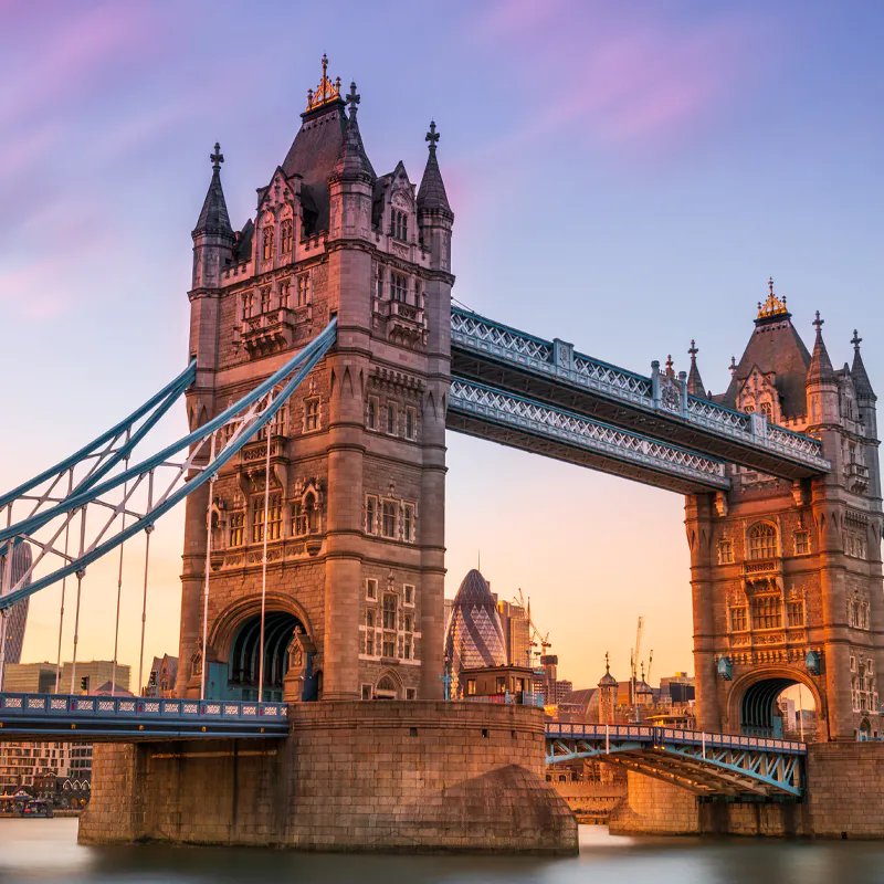 Iconic Tower Bridge in central London with city skyscrapers and River Thames at sunset.