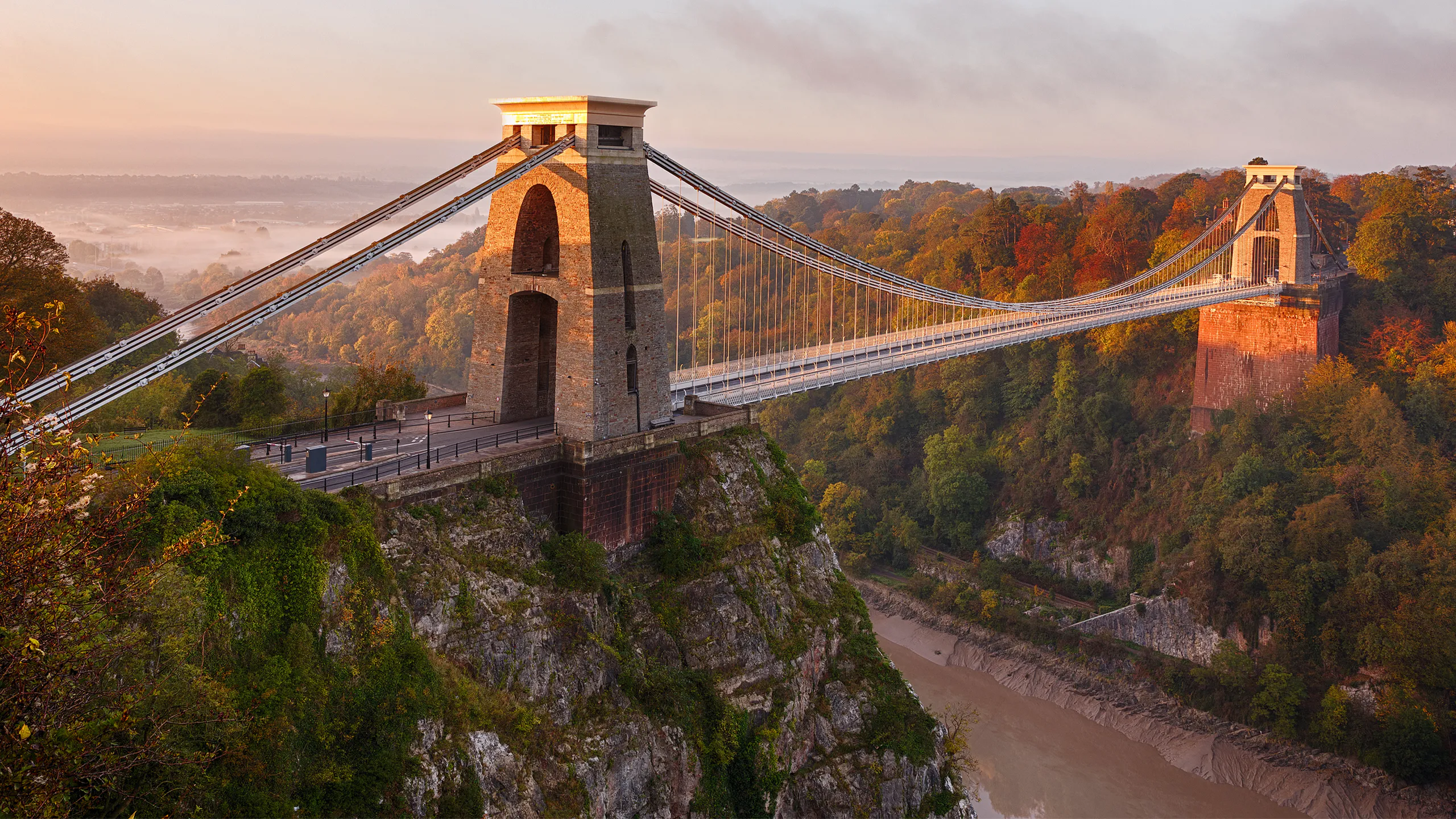 Clifton Suspension Bridge over wooded valley in Bristol, bathed in warm morning light.