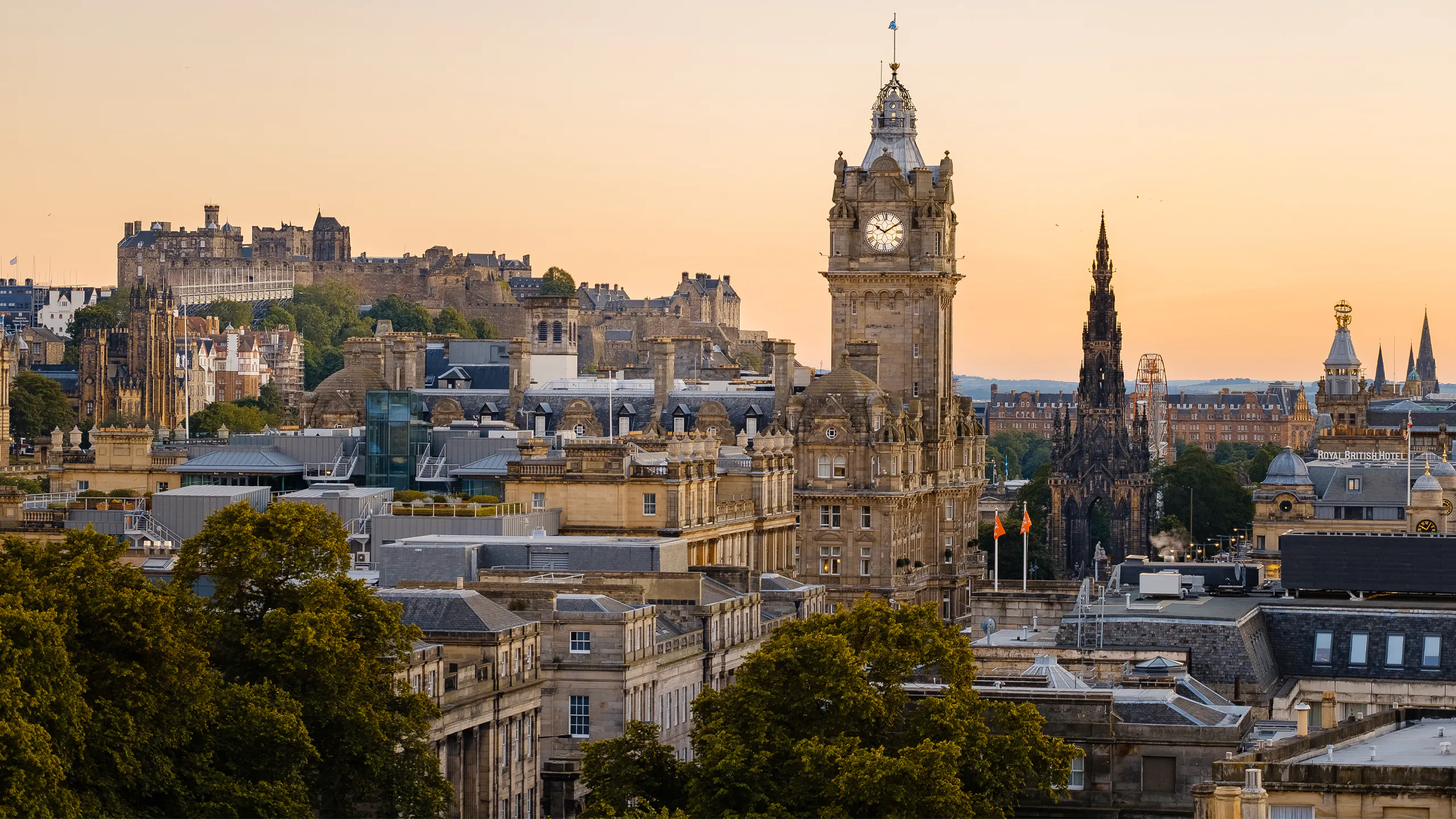 Edinburgh skyline with historic buildings, castle, and Scott Monument at sunset.