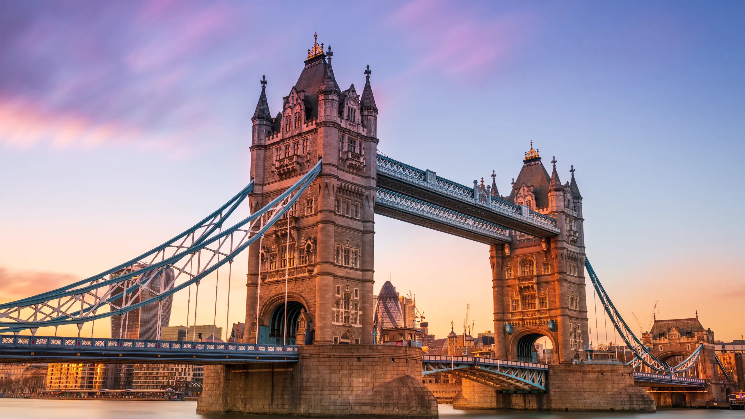 Iconic Tower Bridge in central London with city skyscrapers and River Thames at sunset.